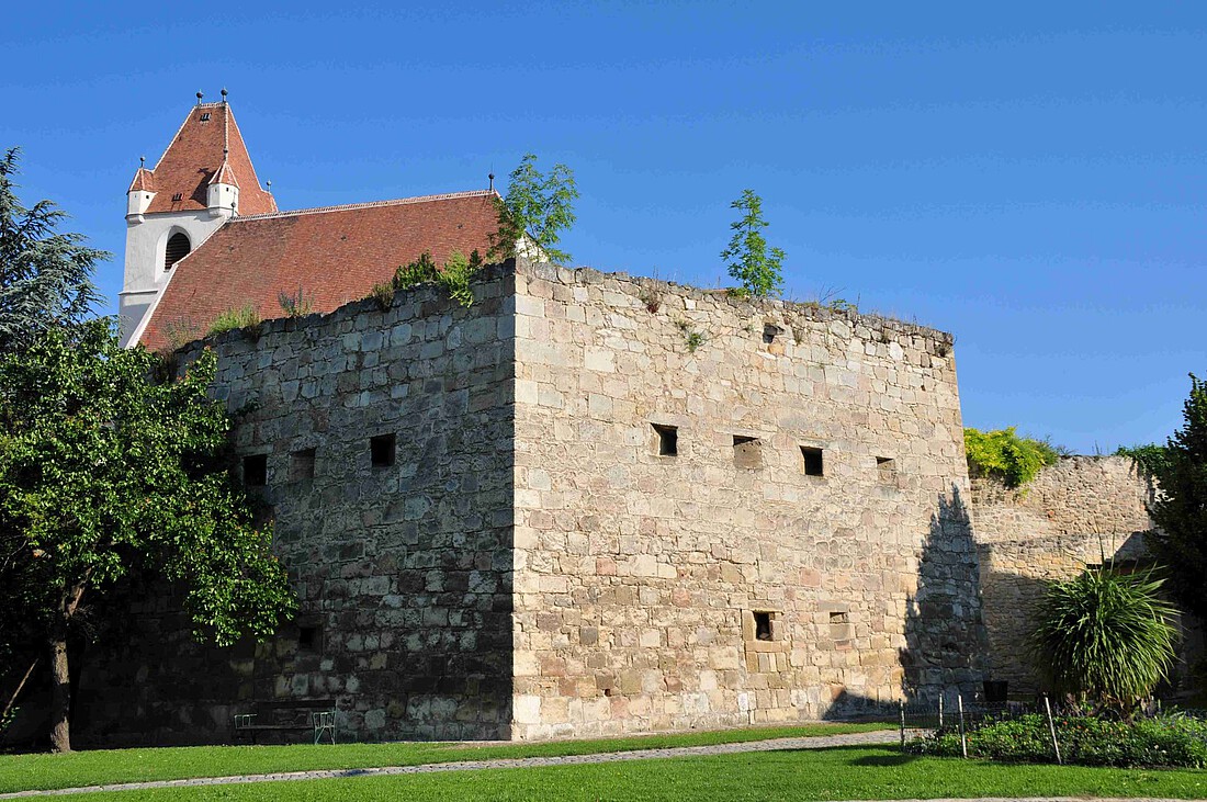 Gut erhaltener Teil einer mittelalterlichen Stadtmauer mit Kirchendach im Hintergrund